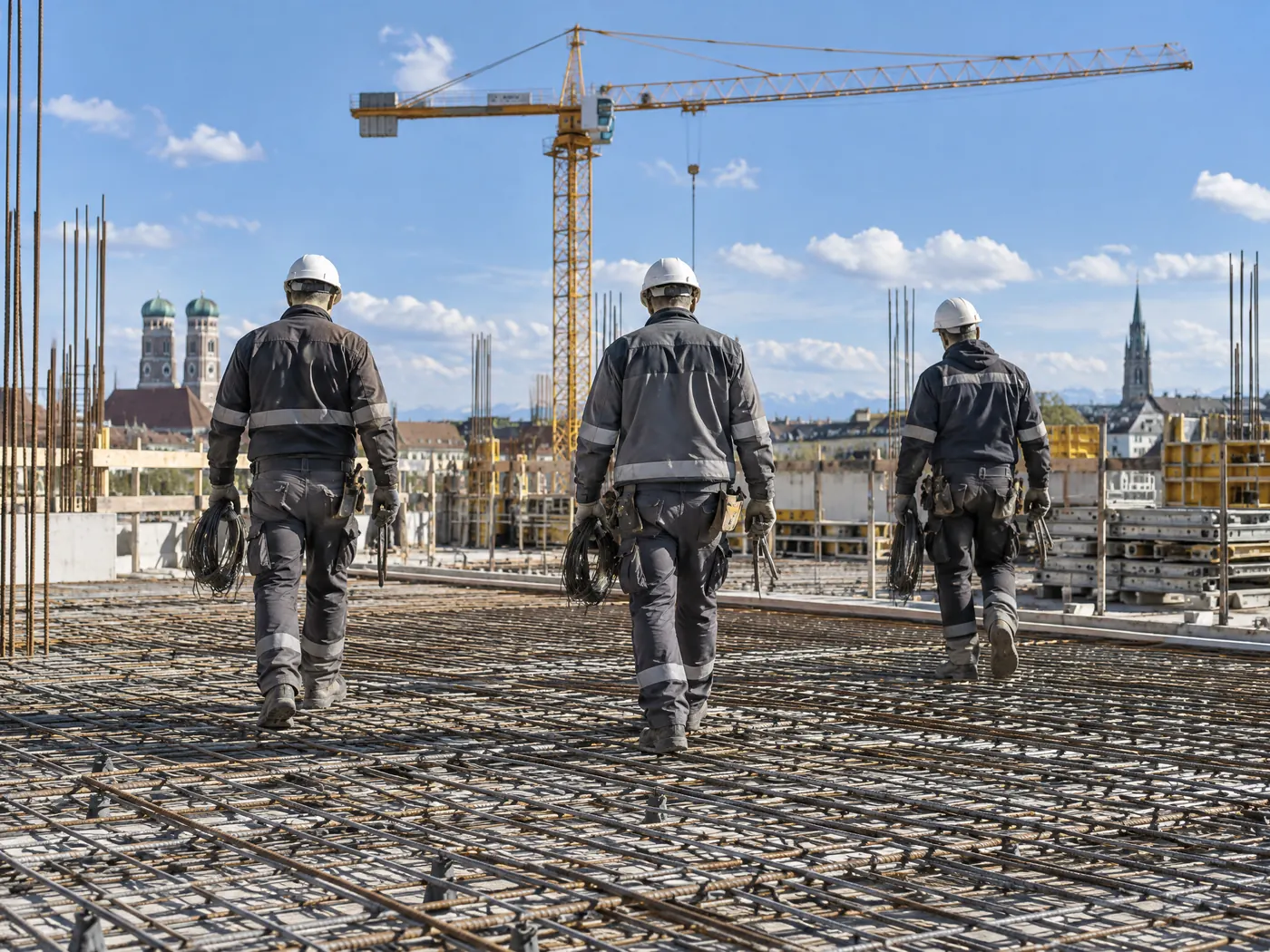 Drei Eisenflechter gehen über eine Bewehrungsmatte auf einer Baustelle in München